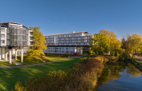 Außenansicht des Hotels, umgeben von einer farbenfrohen Herbstlandschaft mit goldgelben und rötlichen Bäumen.