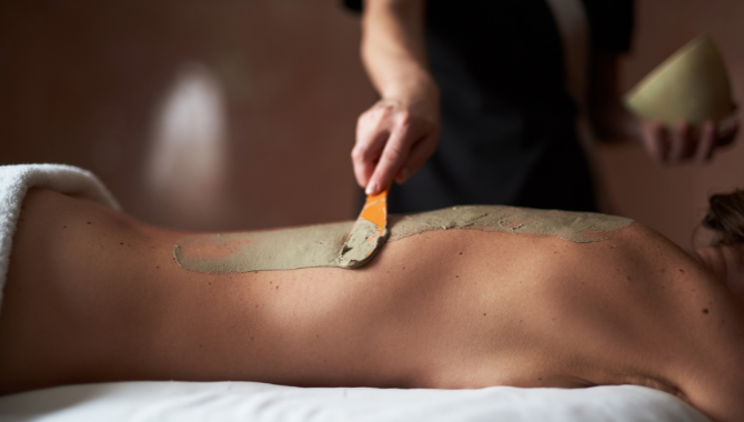 Therapeut trägt eine wohltuende Moorpackung auf den Rücken einer liegenden Person auf.