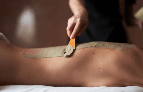 Therapeut trägt eine wohltuende Moorpackung auf den Rücken einer liegenden Person auf.