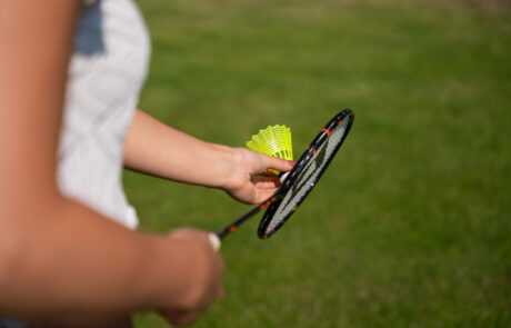 Zusehen ist eine Person die einen Badminton Schläger und einen Federball in der Hand hält
